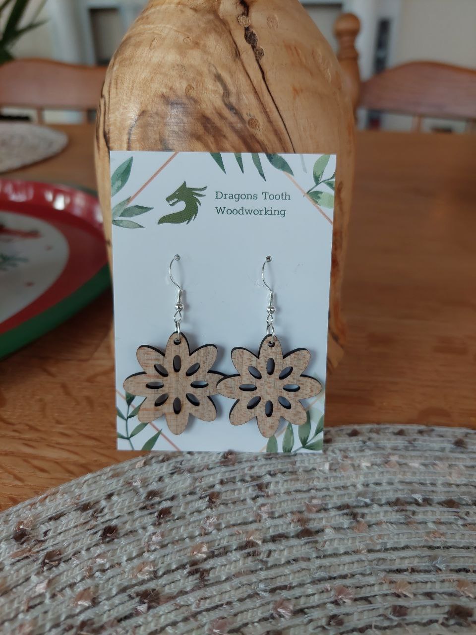 Front view of a pair of maple wood daisy flower cutout silhouette dangle earrings displayed on a rustic earring card.
