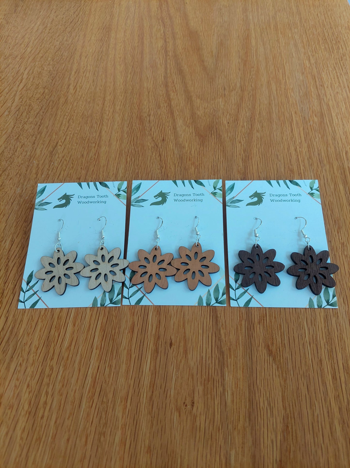 A beautiful collection of handcrafted wooden daisy flower dangle earrings displayed together in natural maple, cherry, and walnut woods.