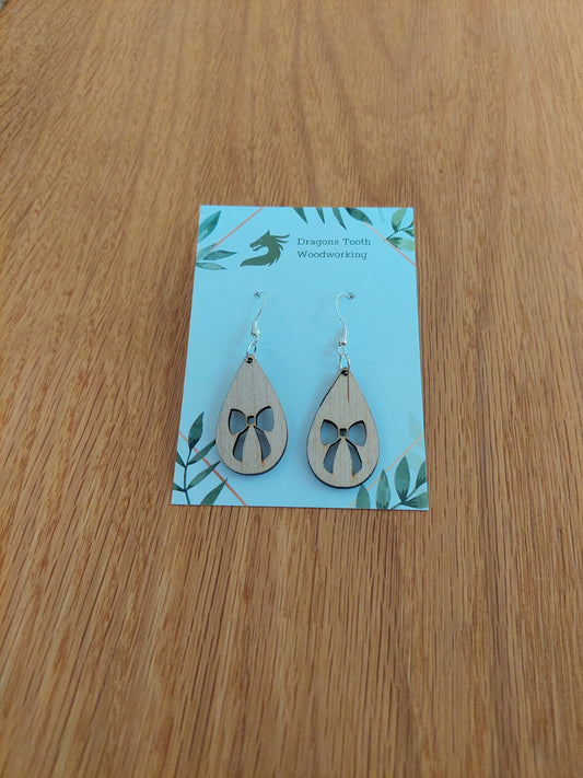 A front view of the ribbon bow teardrop earrings crafted from light, bright blonde solid Maple wood, displayed on an earring card.