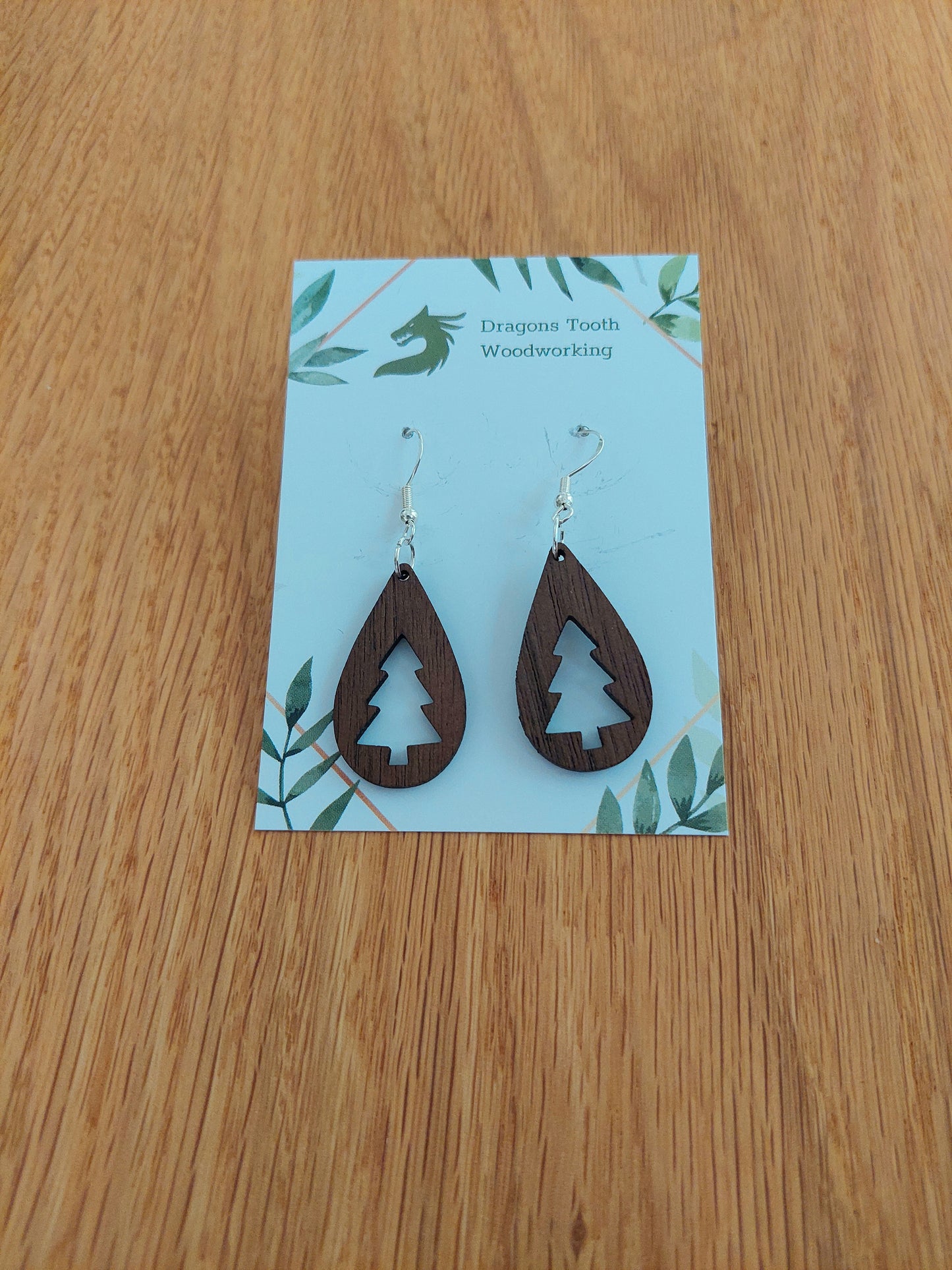 A front view of the Christmas tree teardrop earrings crafted from rich, deep chocolate-brown solid Walnut wood, displayed on an earring card.