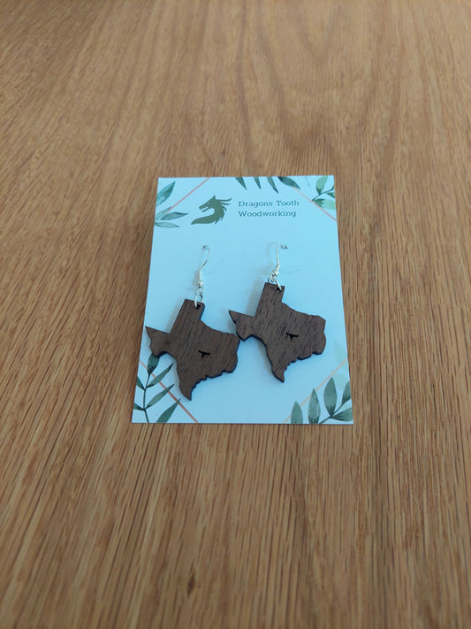 Walnut earrings cut in the shape of the state of Texas with a steer cutout located where the city of Austin is.
