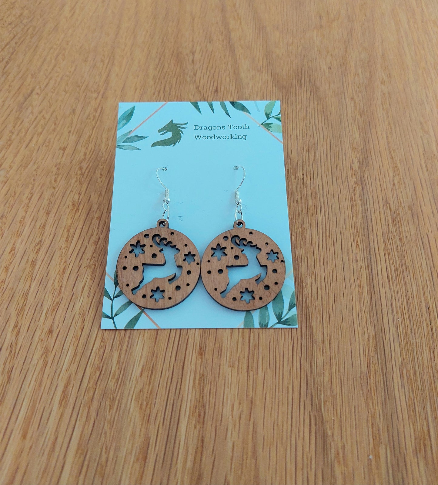 A pair of reindeer earrings made from natural cherry hardwood, displayed on a card with 'Dragon's Tooth Woodworking' written at the top.