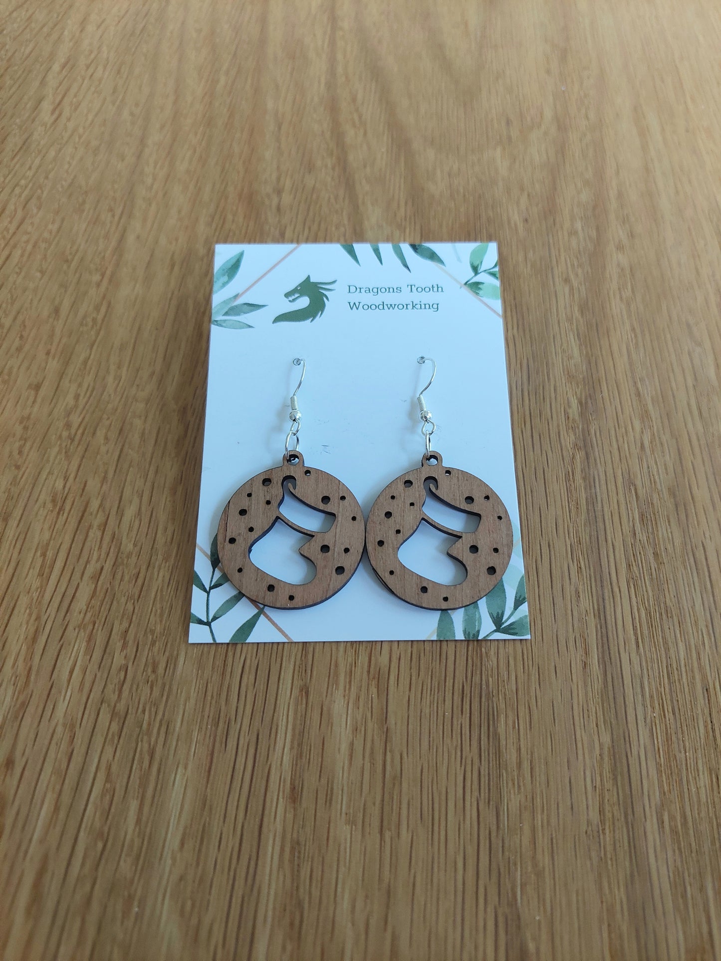 A pair of natural wood earrings featuring Christmas Stockings with hypoallergenic sterling silver plated hooks, displayed on a white card with 'Dragon's Tooth Woodworking' branding.
