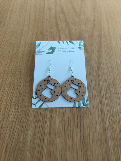 A pair of natural wood earrings featuring Christmas Stockings with hypoallergenic sterling silver plated hooks, displayed on a white card with 'Dragon's Tooth Woodworking' branding.