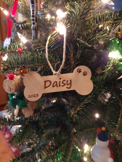 Custom engraved dog bone Christmas ornament made of birch wood with red ribbon, personalized with pet’s name for holiday decor.