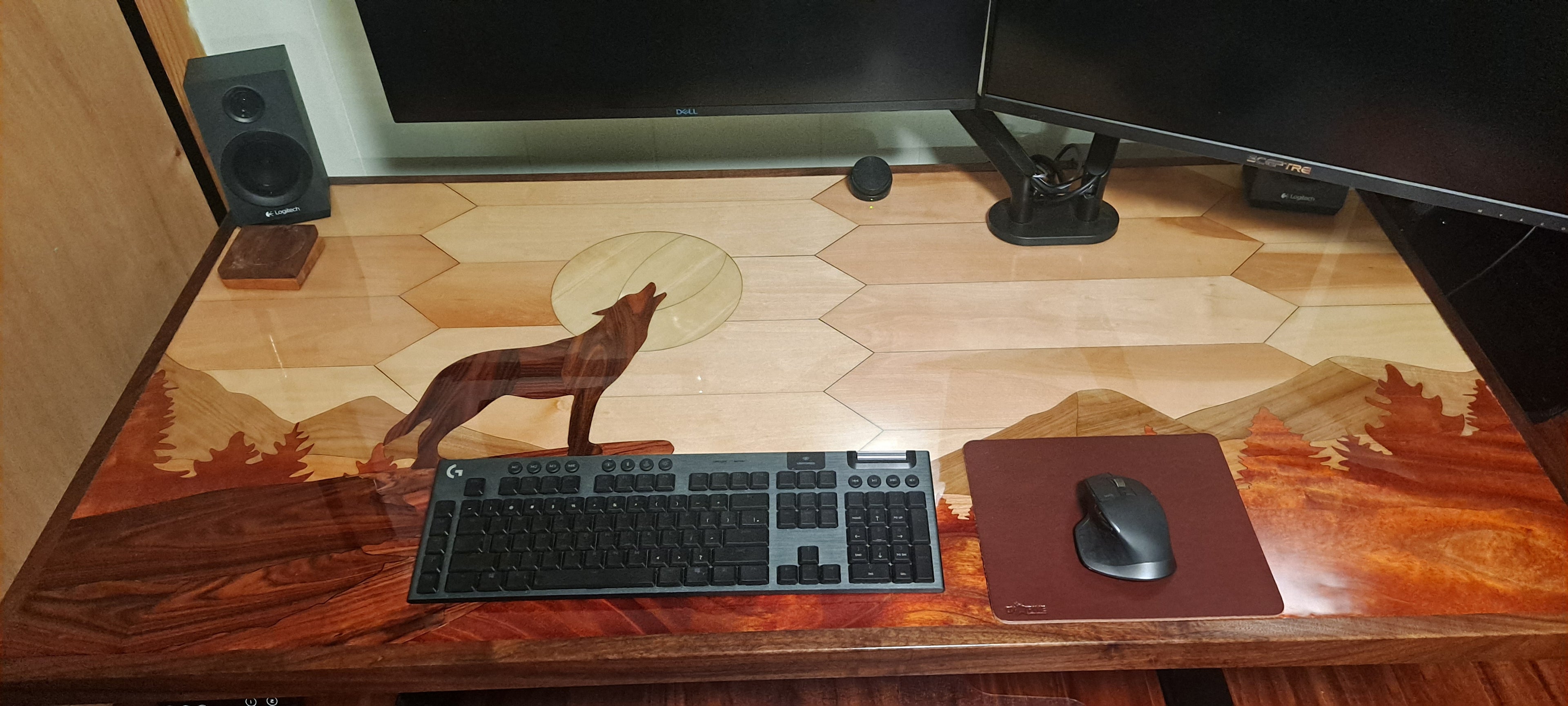 Desktop surface made with inlay marquetry style to form a view of a wolf howling at the moon with mountains in the back ground. It features aspen, birch, butternut, mahogany, Brazilian rosewood, cherry and black walnut.