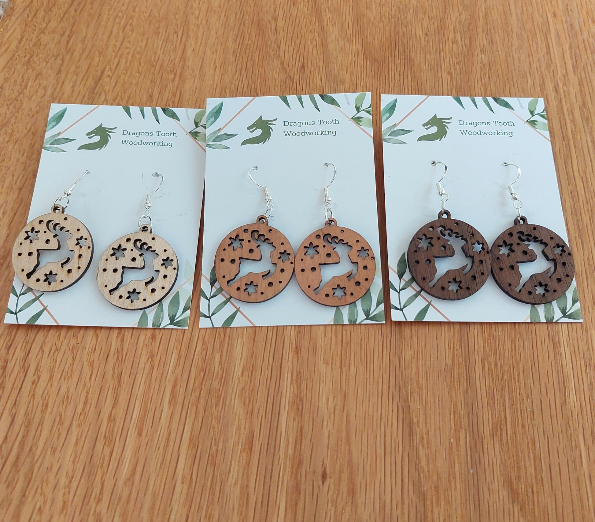 Pairs of reindeer earrings made from natural hardwoods, with silver hooks displayed on a card with 'Dragon's Tooth Woodworking' written at the top.