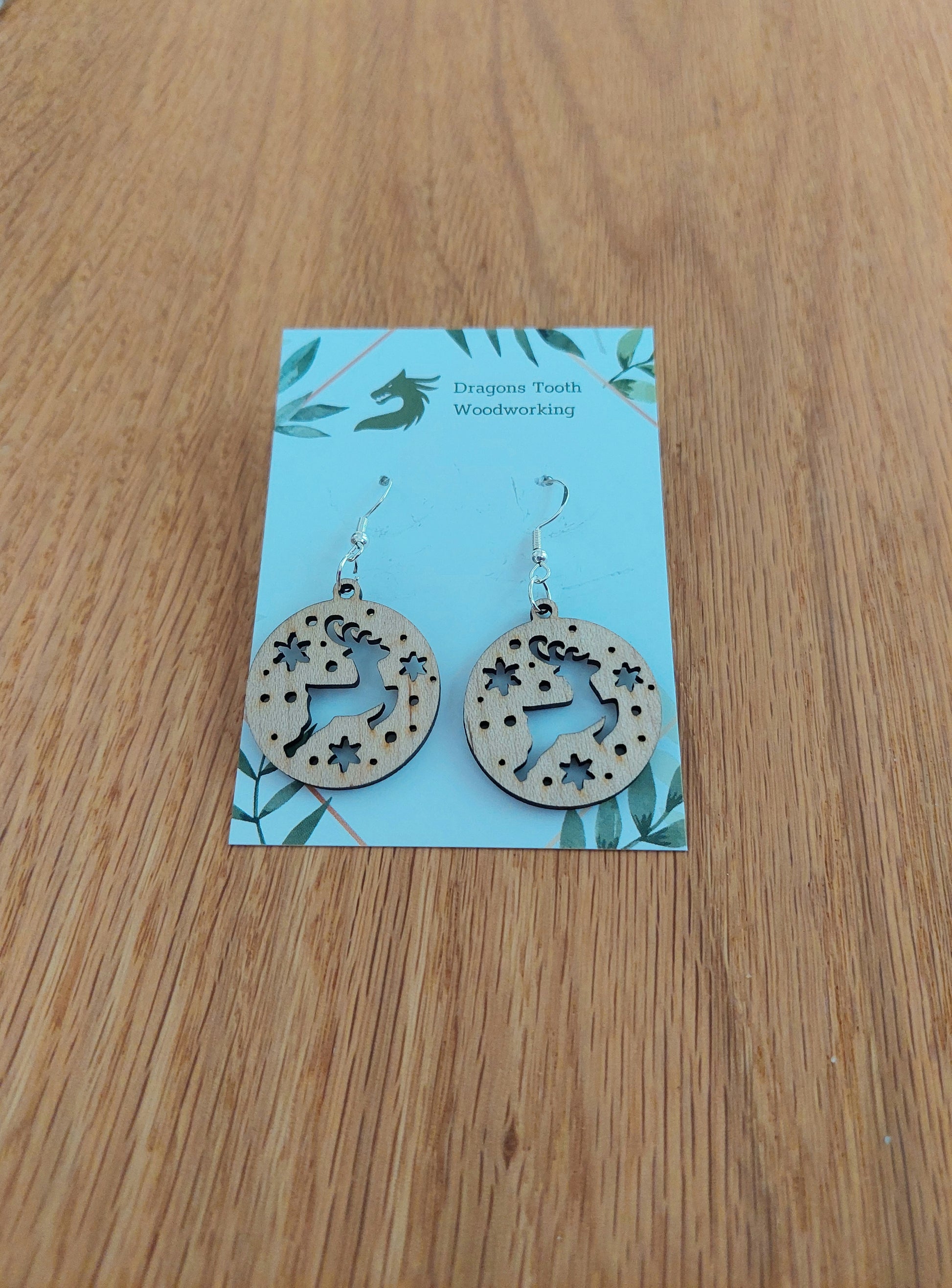 A pair of reindeer earrings made from natural maple hardwood, displayed on a card with 'Dragon's Tooth Woodworking' written at the top.