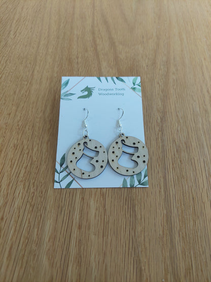 A pair of natural wood earrings featuring Christmas Stockings with hypoallergenic sterling silver plated hooks, displayed on a white card with 'Dragon's Tooth Woodworking' branding.
