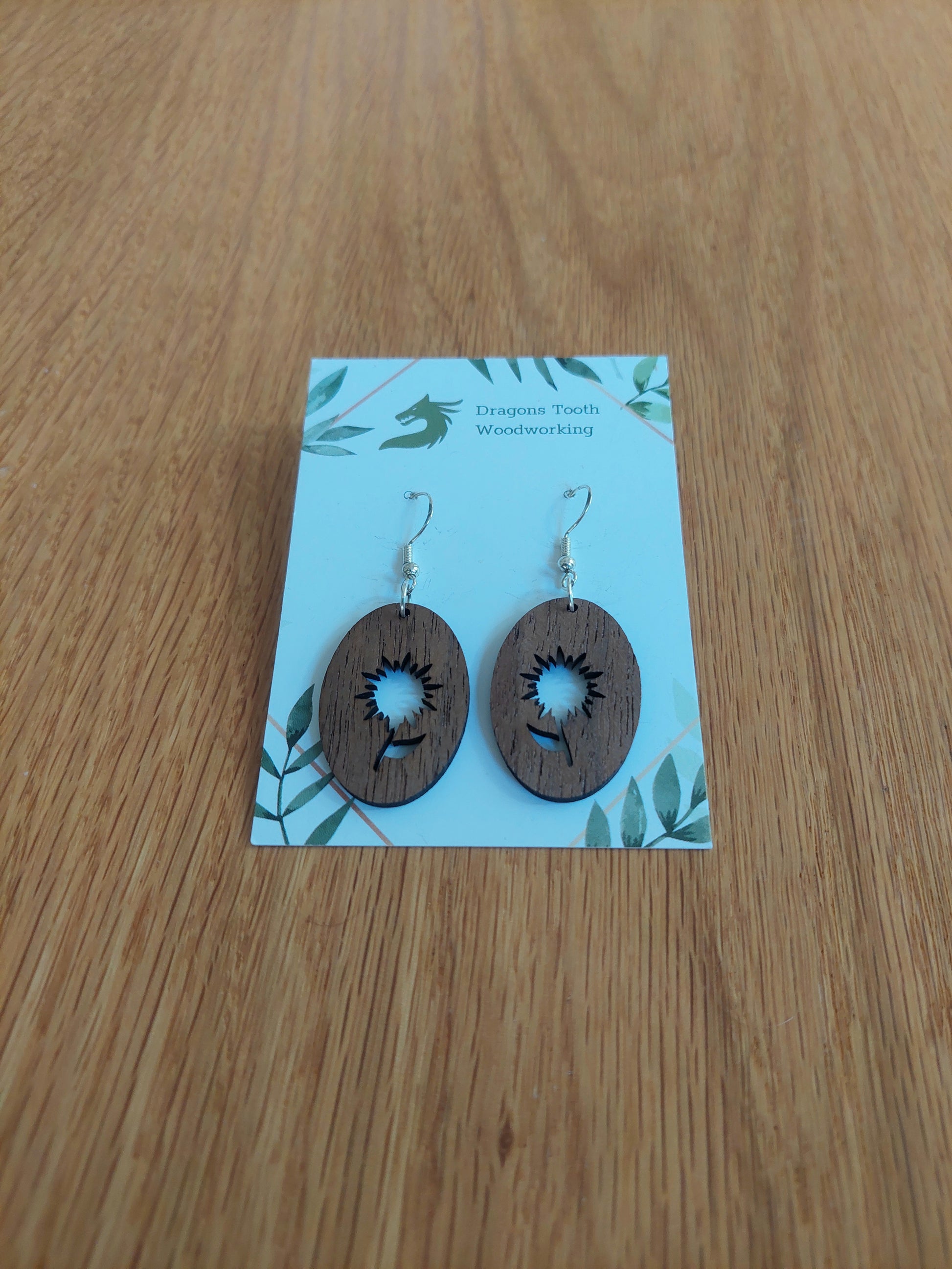 A front view of the aster flower earrings crafted from rich, deep chocolate-brown solid Walnut wood, displayed on an earring card.