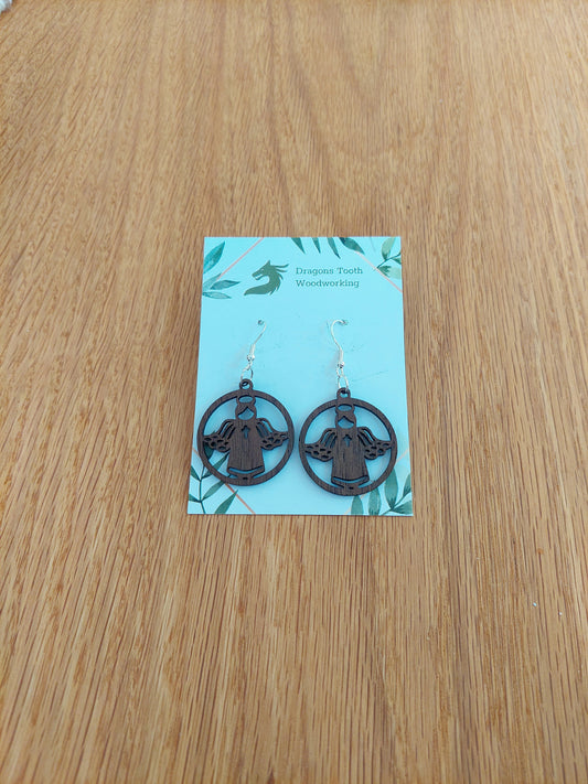 A pair of dark brown chocolate colored walnut wood angel earrings displayed with silver hooks on a card with the brand name 'Dragon's Tooth Woodworking'.