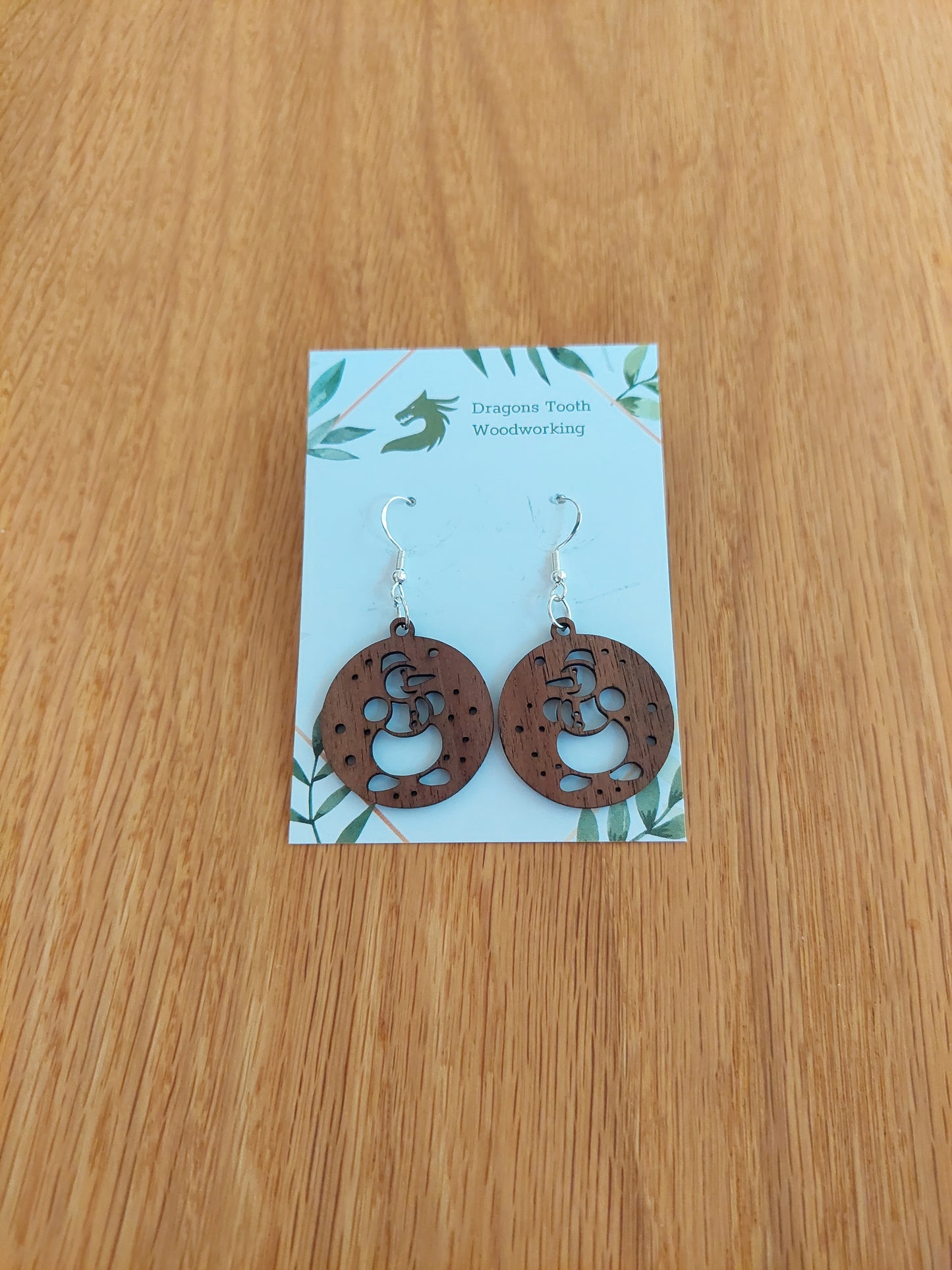 A pair of snowman-shaped earrings made from natural black walnut, displayed on a card