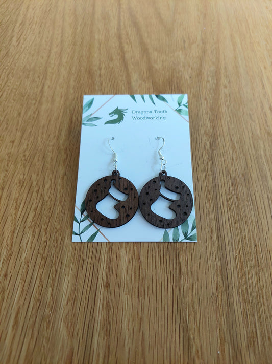 A pair of natural wood earrings featuring Christmas Stockings with hypoallergenic sterling silver plated hooks, displayed on a white card with 'Dragon's Tooth Woodworking' branding.