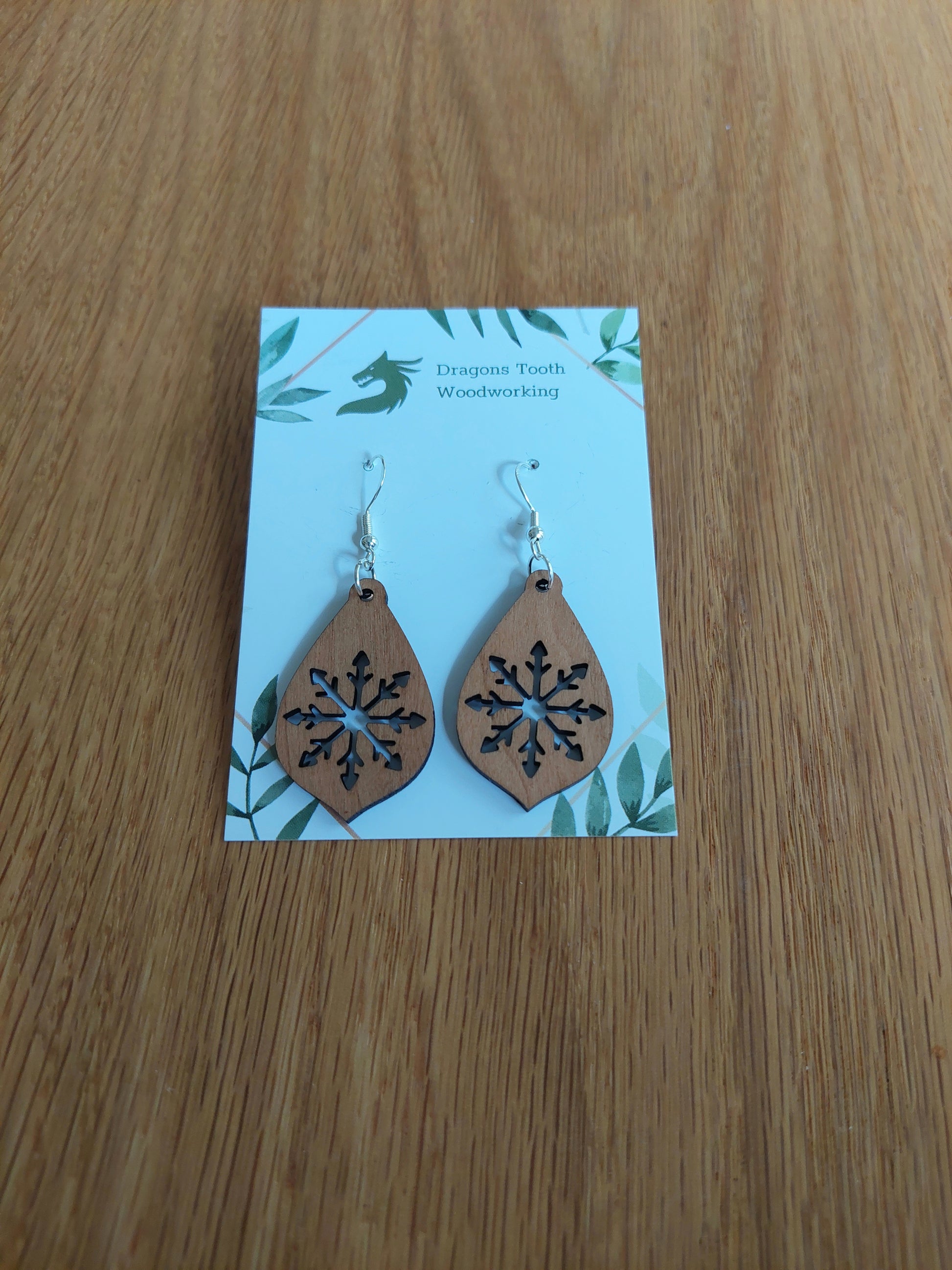 A front view of the large snowflake teardrop earrings crafted from warm, traditional caramel-toned solid Cherry wood, displayed on an earring card.