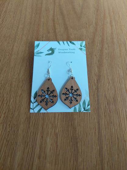 A front view of the large snowflake teardrop earrings crafted from warm, traditional caramel-toned solid Cherry wood, displayed on an earring card.