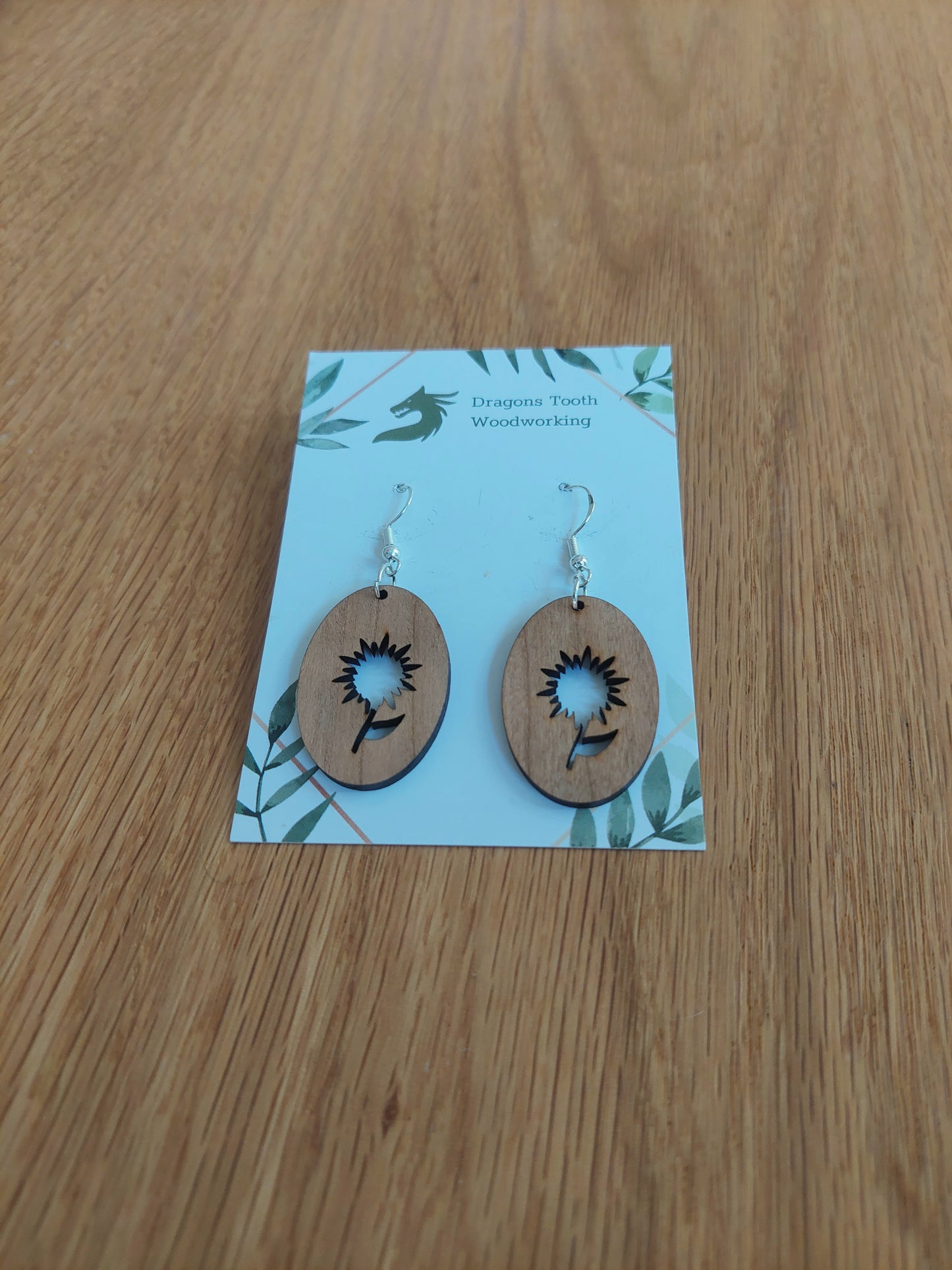 A front view of the aster flower earrings crafted from warm, traditional caramel-toned solid Cherry wood, displayed on an earring card.
