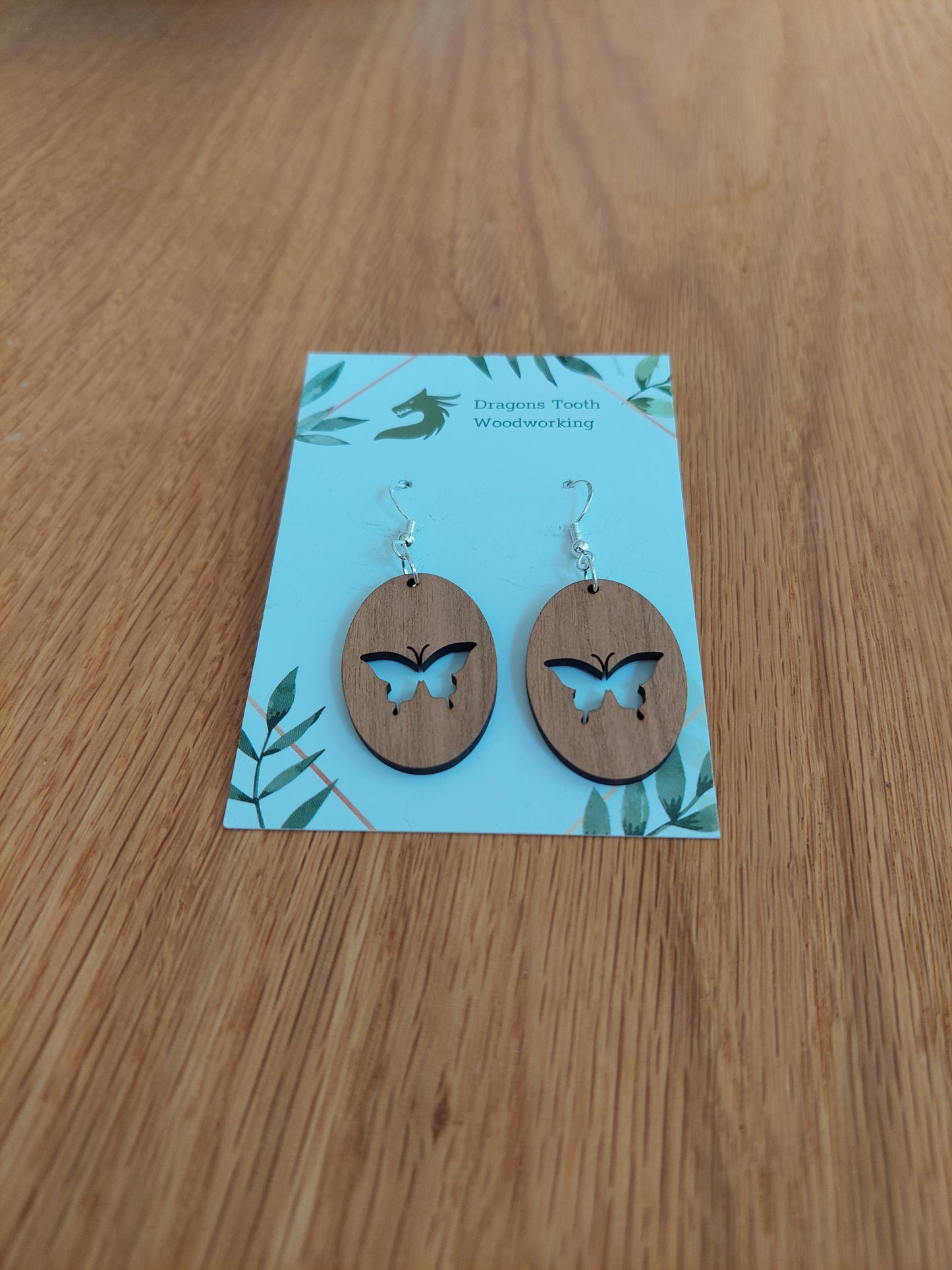 A front view of the butterfly earrings crafted from warm, traditional caramel-toned solid Cherry wood, displayed on an earring card.