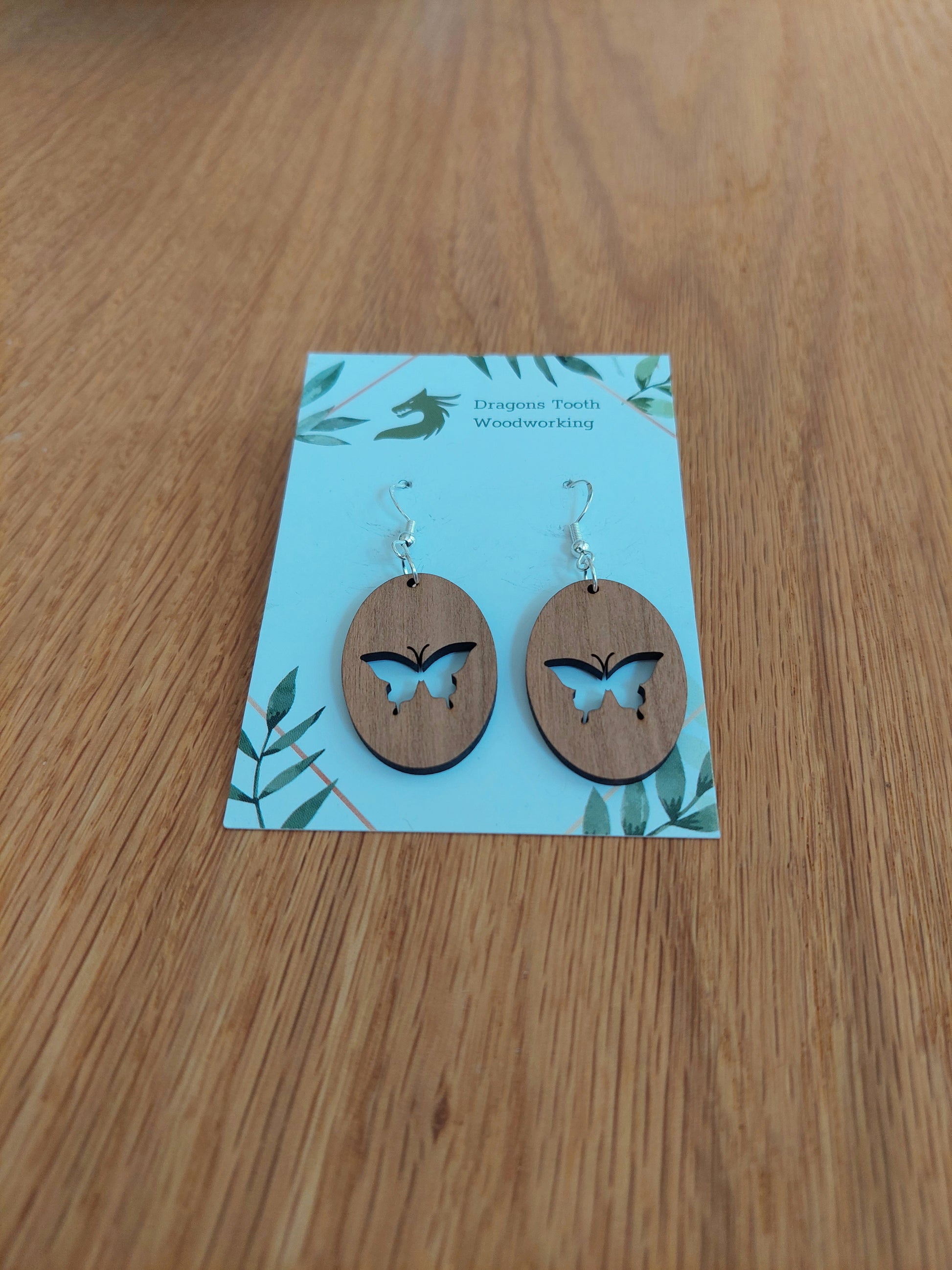 A front view of the butterfly earrings crafted from warm, traditional caramel-toned solid Cherry wood, displayed on an earring card.