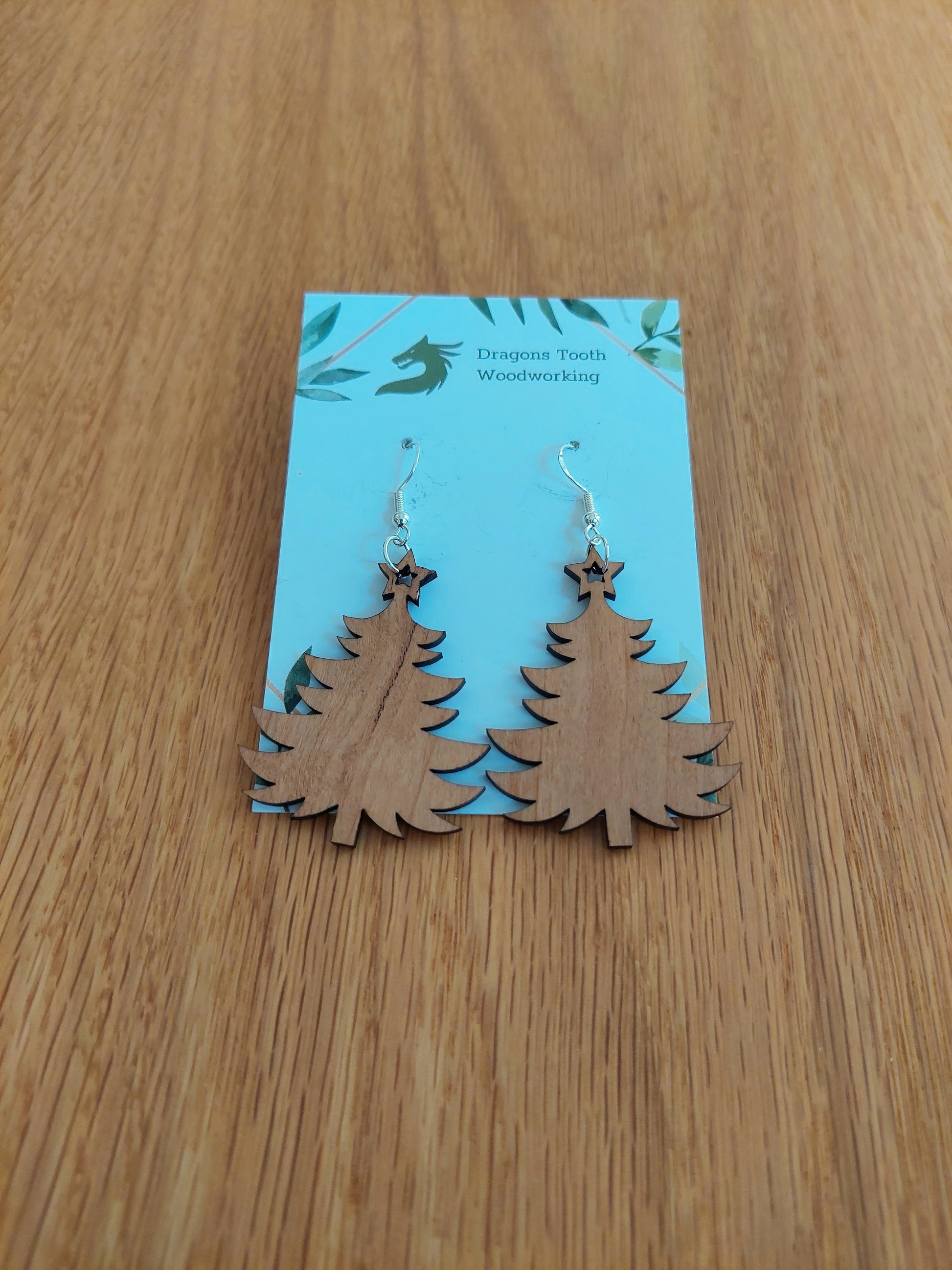 A front view of the Christmas tree earrings crafted from warm, traditional caramel-toned solid Cherry wood, displayed on an earring card.