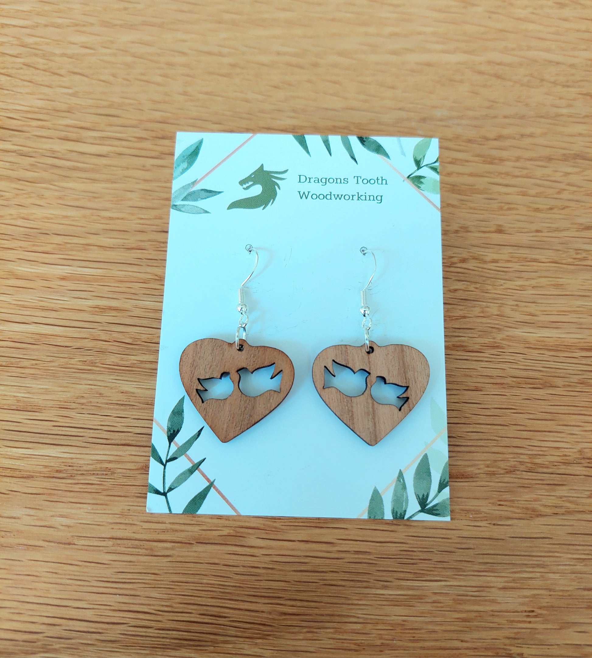 A front view of the minimalist dove earrings crafted from warm, traditional caramel-toned solid Cherry wood, displayed on an earring card.