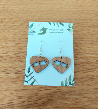A front view of the minimalist dove earrings crafted from warm, traditional caramel-toned solid Cherry wood, displayed on an earring card.