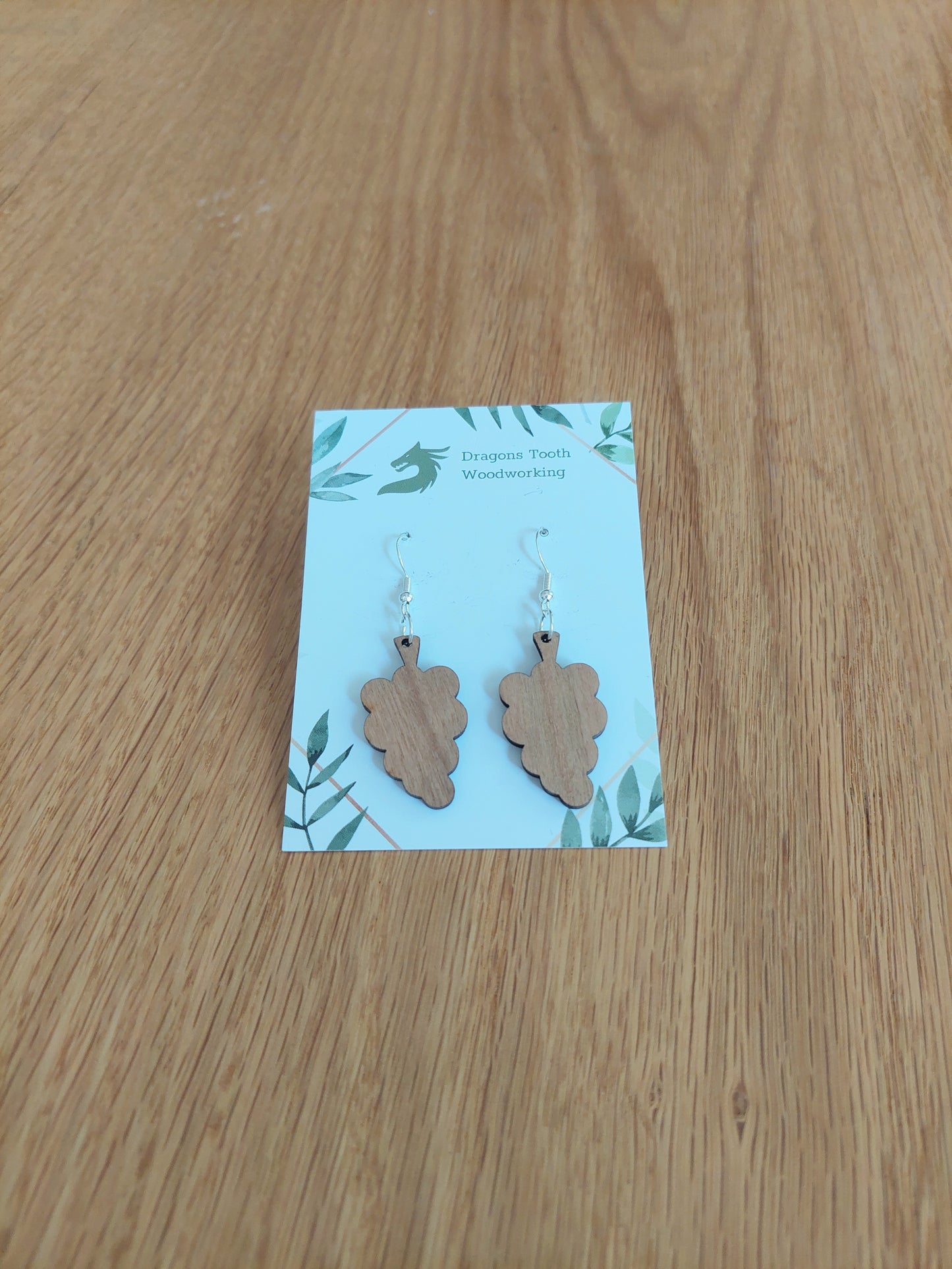 A front view of the grape cluster earrings crafted from warm, traditional caramel-toned solid Cherry wood, displayed on an earring card.