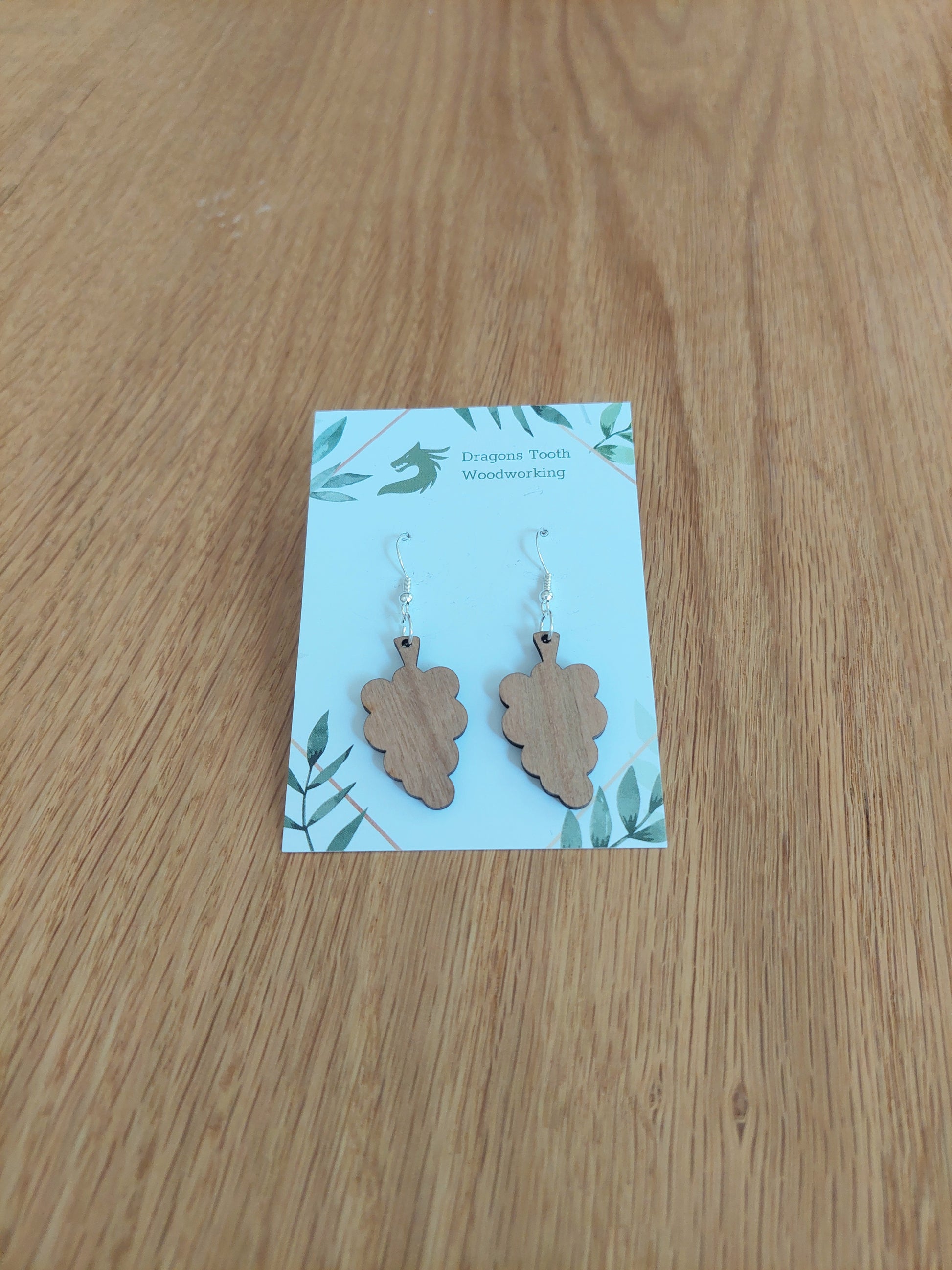 A front view of the grape cluster earrings crafted from warm, traditional caramel-toned solid Cherry wood, displayed on an earring card.