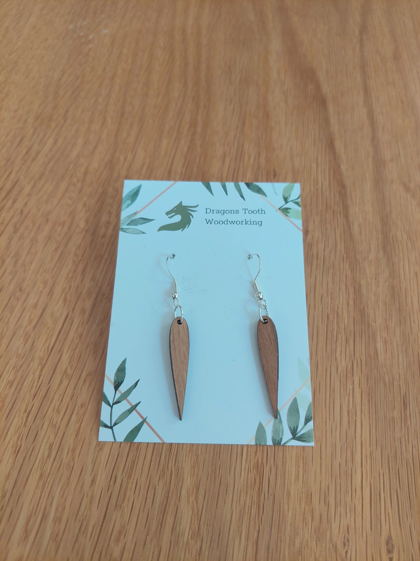 A front view of the minimalist pointed geometric earrings crafted from warm, traditional caramel-toned solid Cherry wood, displayed on an earring card.