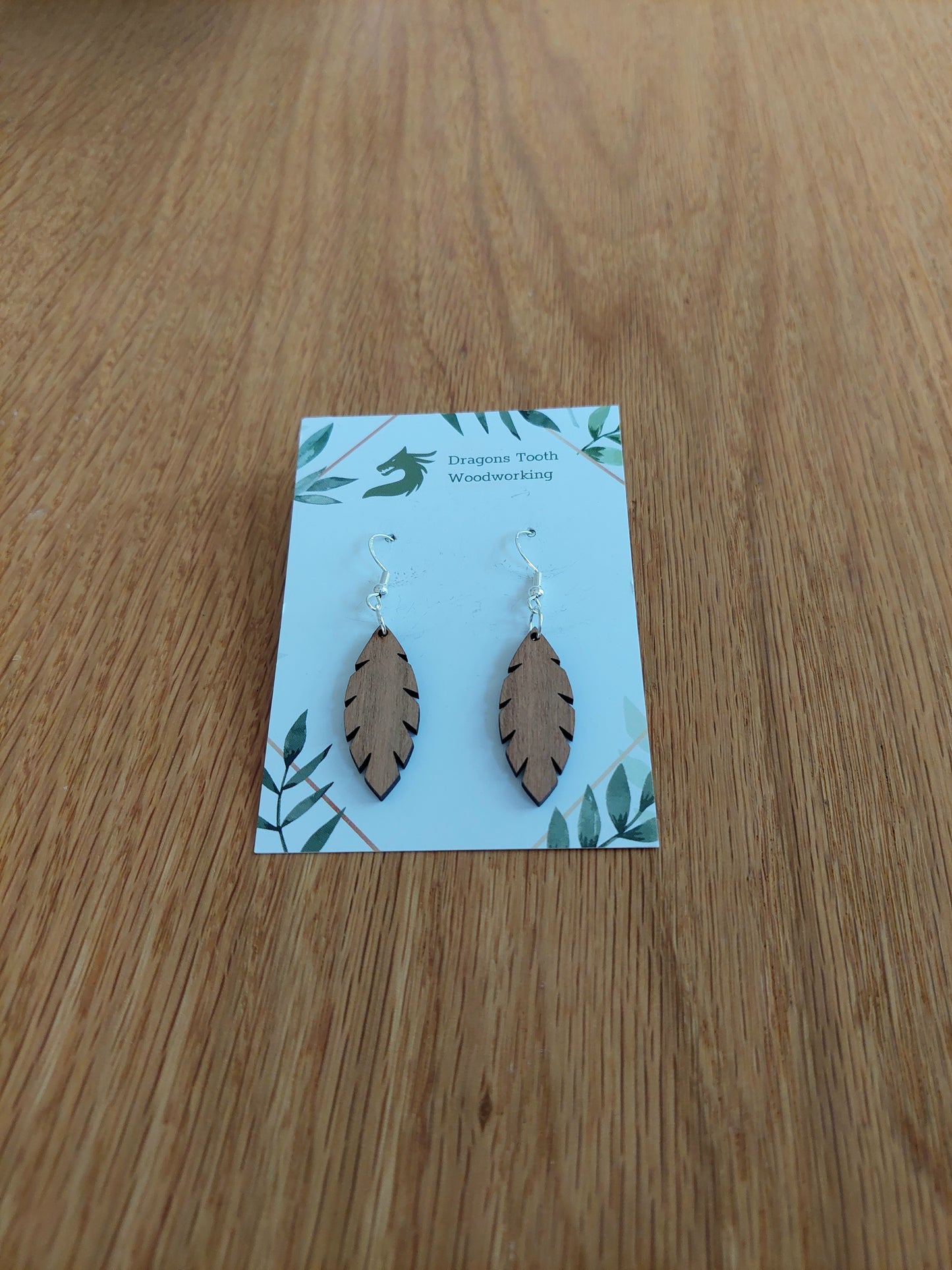 A front view of the minimalist simple leaf earrings crafted from warm, traditional caramel-toned solid Cherry wood, displayed on an earring card.