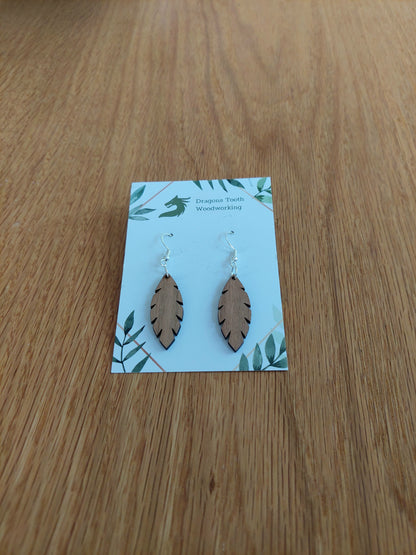 A front view of the minimalist simple leaf earrings crafted from warm, traditional caramel-toned solid Cherry wood, displayed on an earring card.