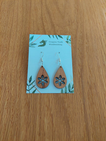 A front view of the snowflake teardrop earrings crafted from warm, traditional caramel-toned solid Cherry wood, displayed on an earring card.