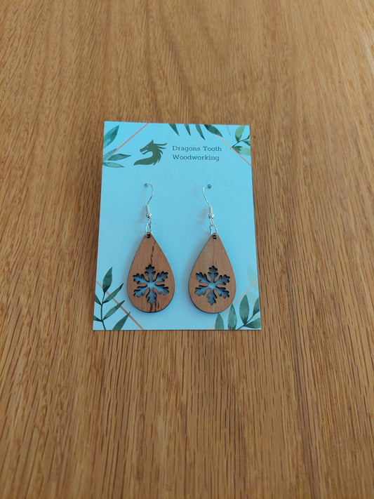 A front view of the snowflake teardrop earrings crafted from warm, traditional caramel-toned solid Cherry wood, displayed on an earring card.
