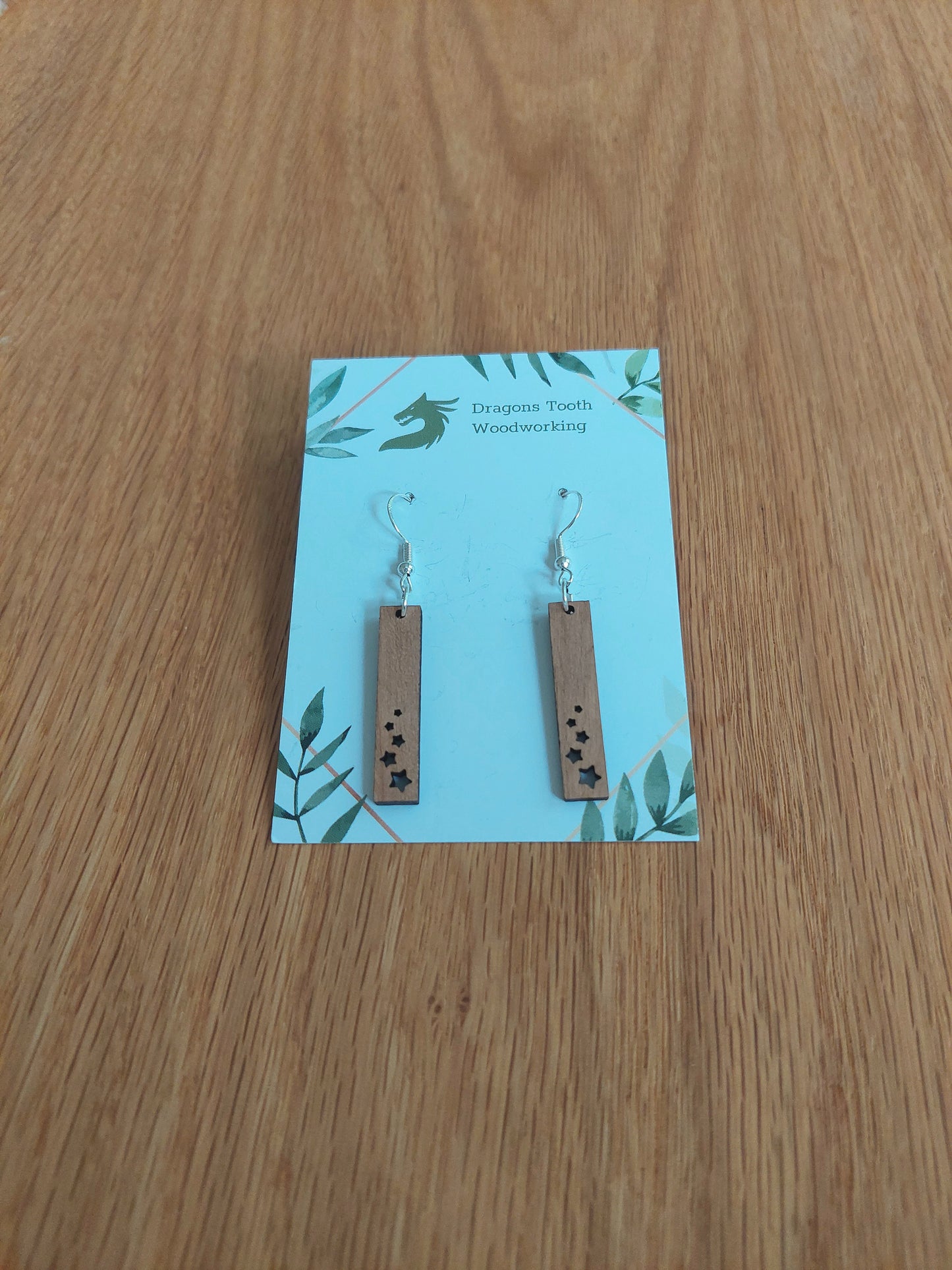 A front view of the minimalist star shower earrings crafted from warm, traditional caramel-toned solid Cherry wood, displayed on an earring card.