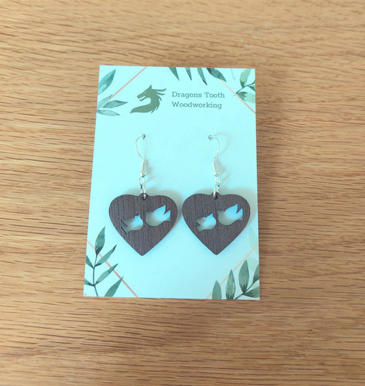 Front view of a pair of walnut wood Christian peace dove silhouette dangle earrings displayed on a rustic earring card
