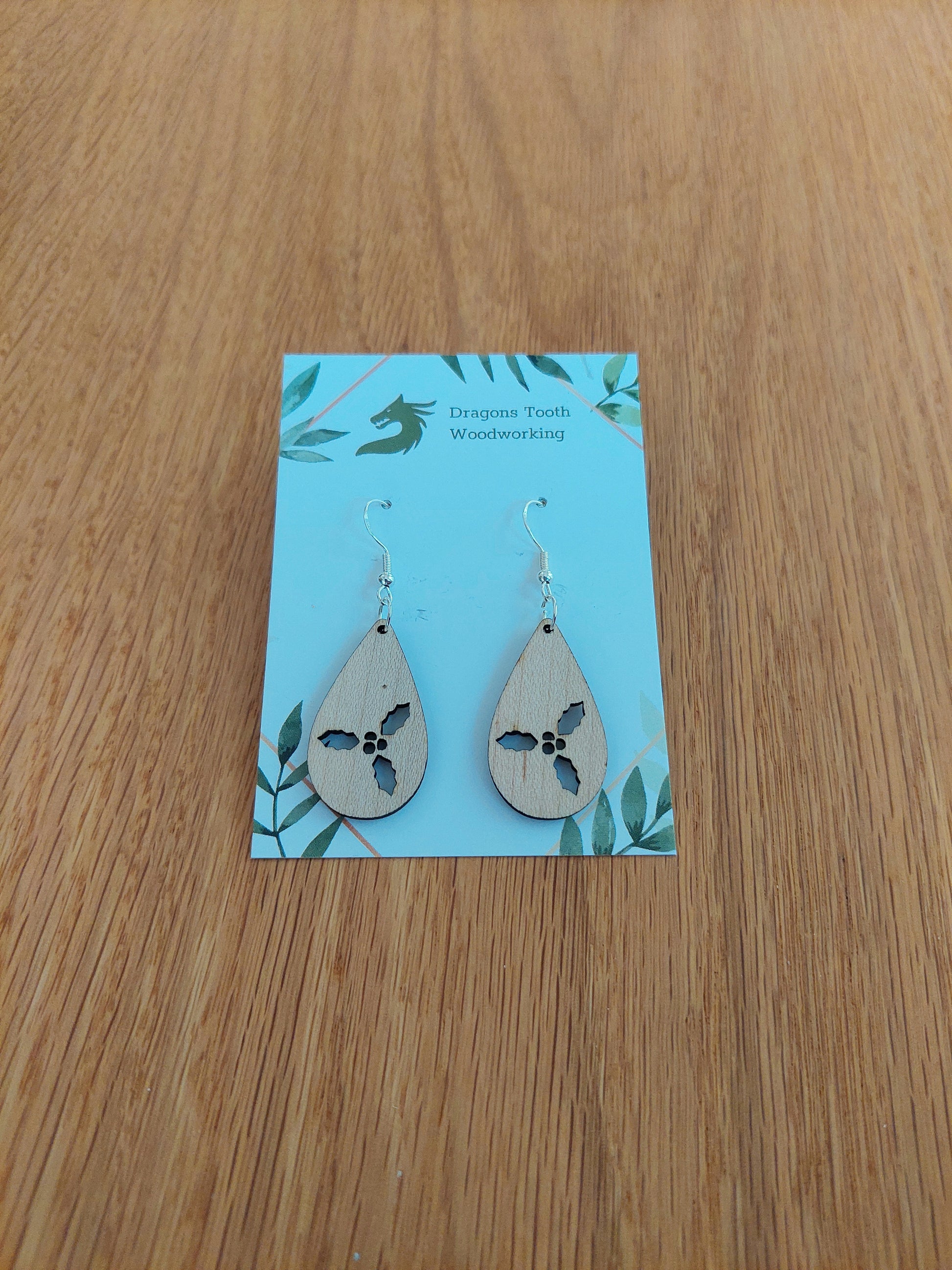 Front view of a pair of maple wood holly cluster teardrop dangle earrings on an earring display card