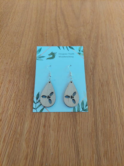 Front view of a pair of maple wood holly cluster teardrop dangle earrings on an earring display card