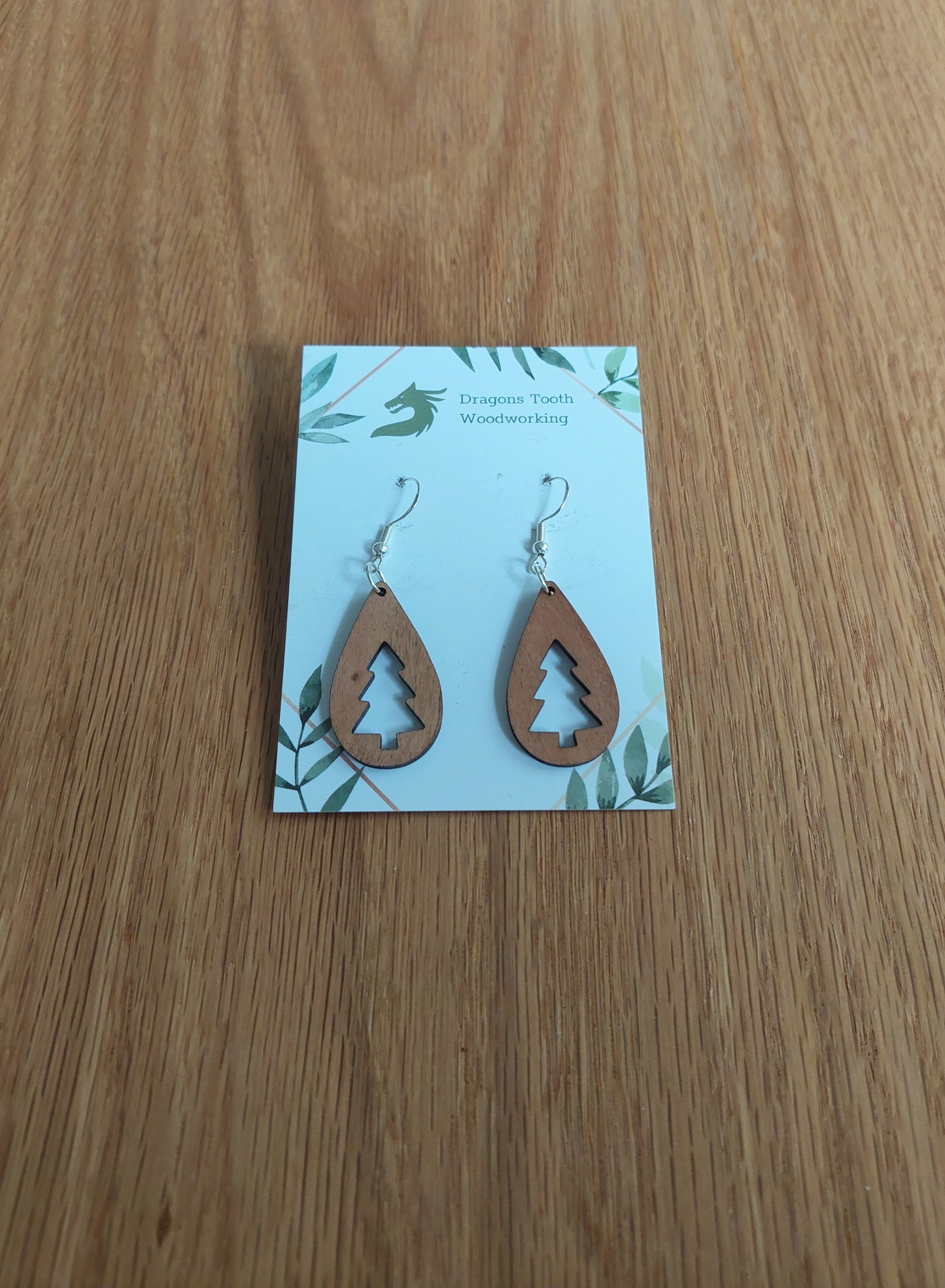 Front view of a pair of cherry wood Christmas tree teardrop dangle earrings displayed on a rustic earring card.