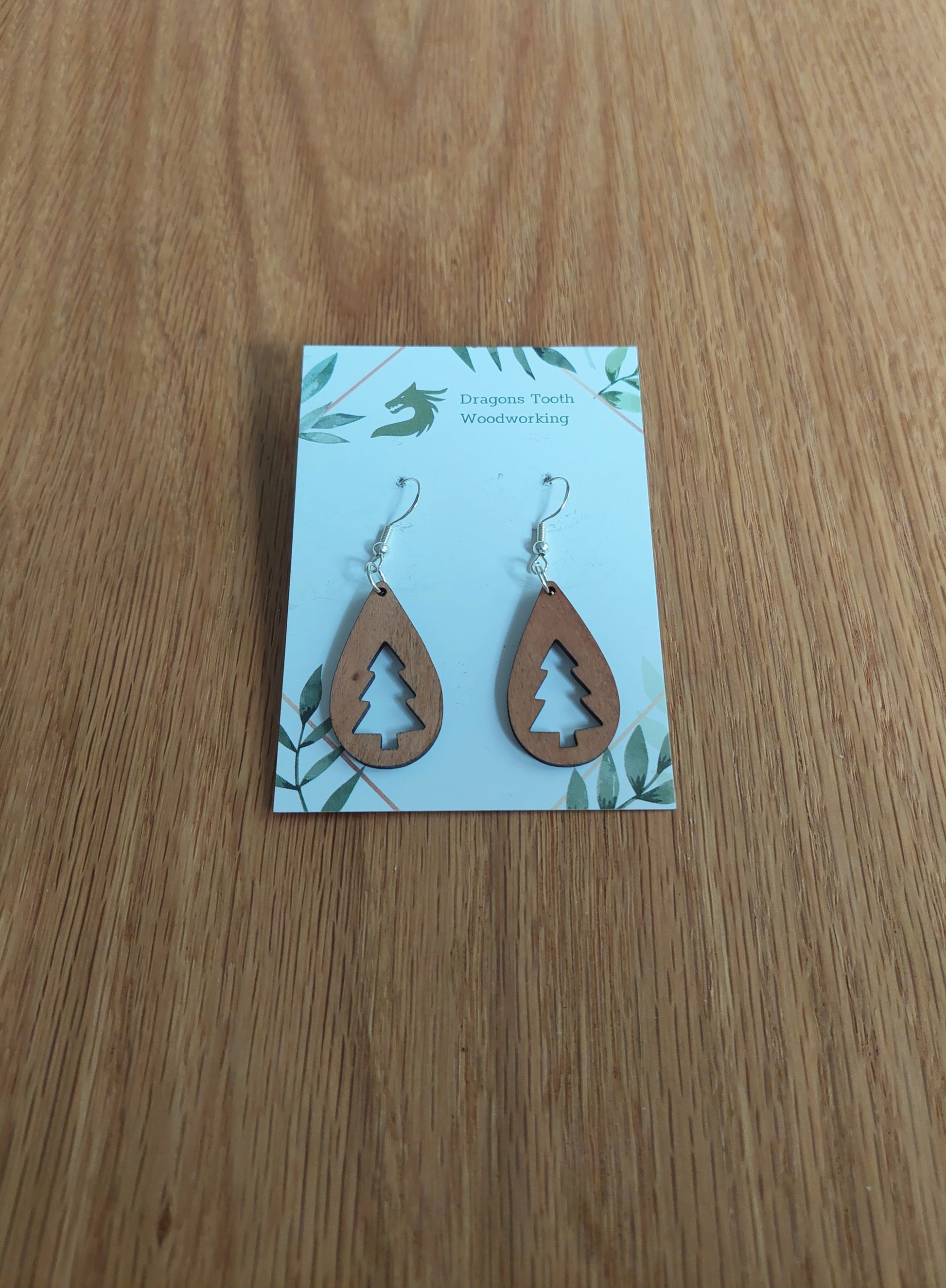 Front view of a pair of cherry wood Christmas tree teardrop dangle earrings displayed on a rustic earring card.