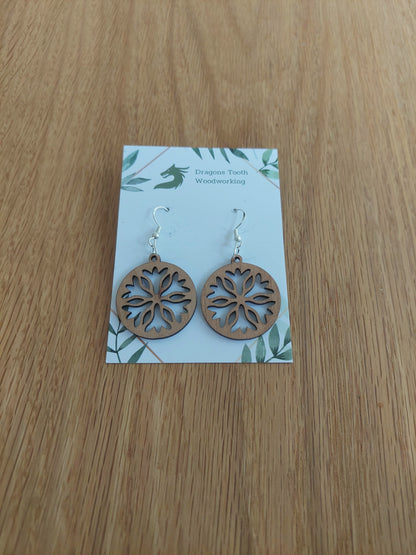 Front view of a pair of cherry wood classic snowflake silhouette dangle earrings displayed on a rustic earring card