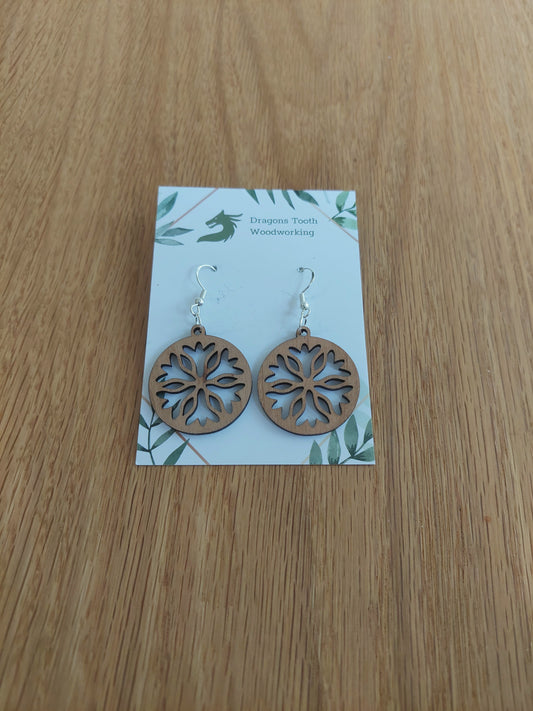 Front view of a pair of cherry wood classic snowflake silhouette dangle earrings displayed on a rustic earring card