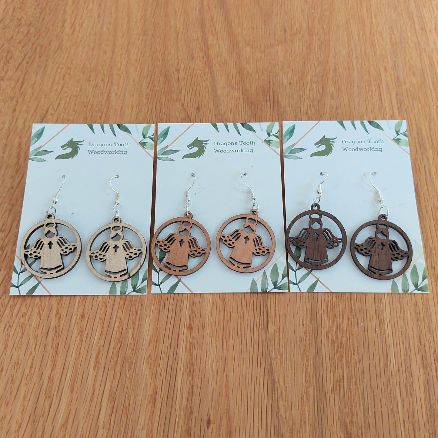 A beautiful collection of handcrafted wooden angel dangle earrings displayed together in natural maple, cherry, and walnut hardwood finishes.