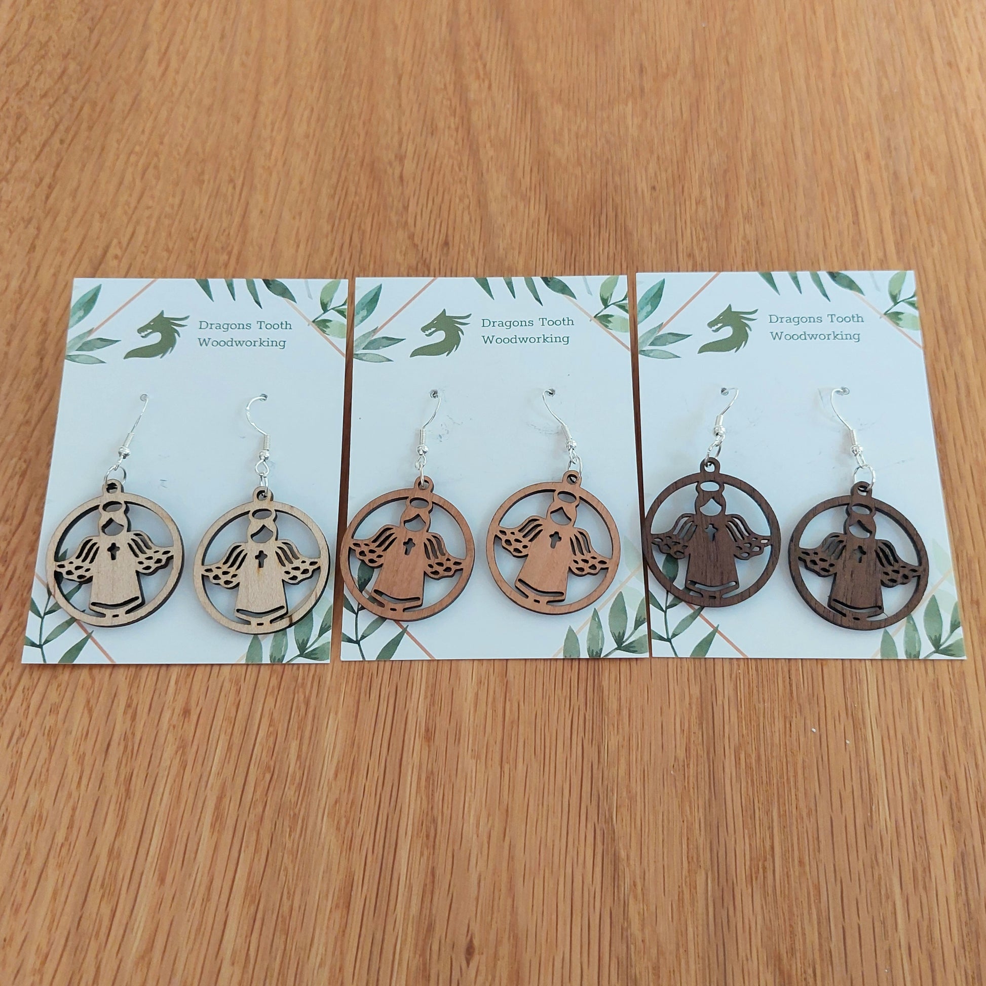 A beautiful collection of handcrafted wooden angel dangle earrings displayed together in natural maple, cherry, and walnut hardwood finishes.