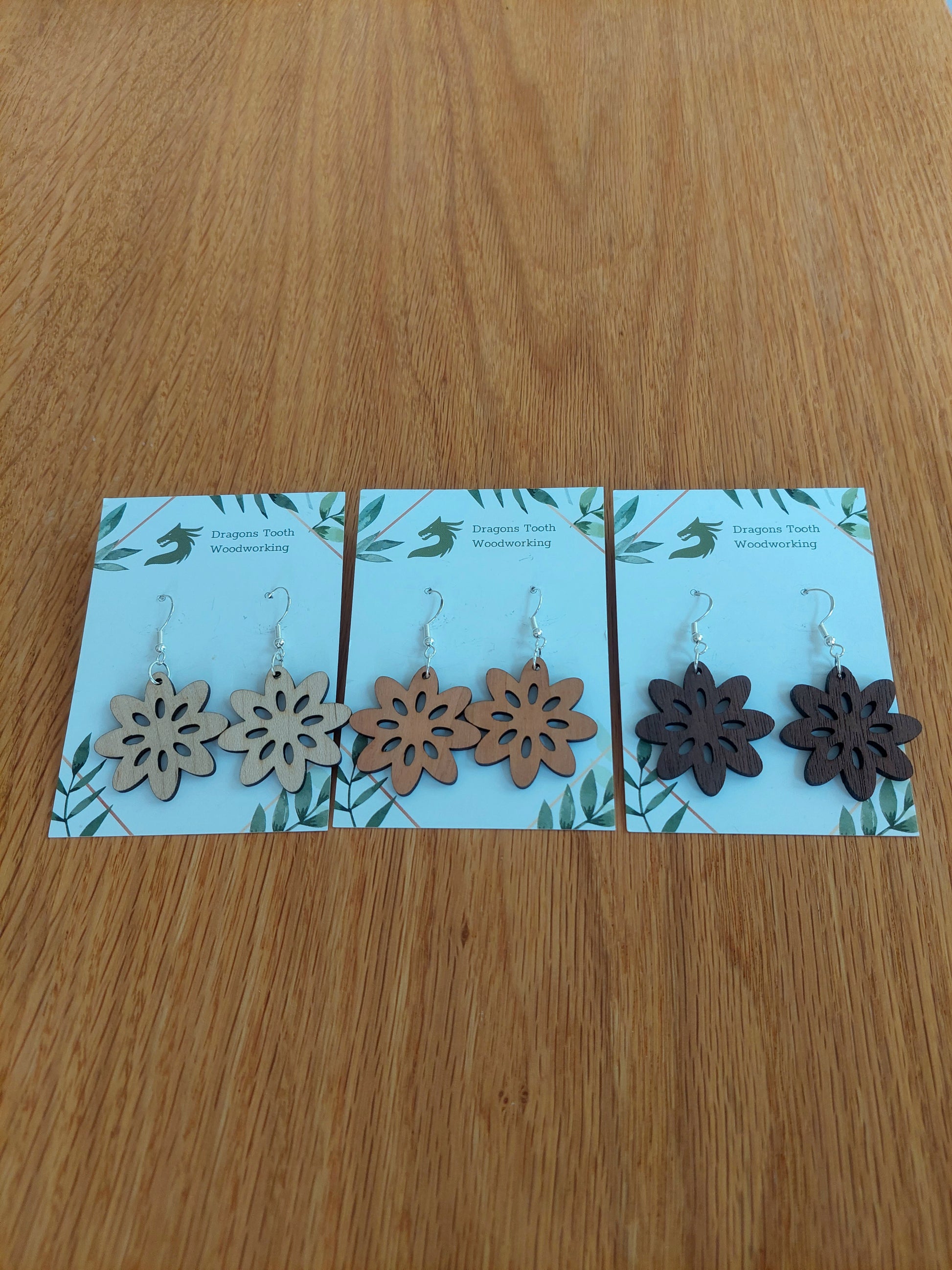 A beautiful collection of handcrafted wooden daisy flower dangle earrings displayed together in natural maple, cherry, and walnut woods.