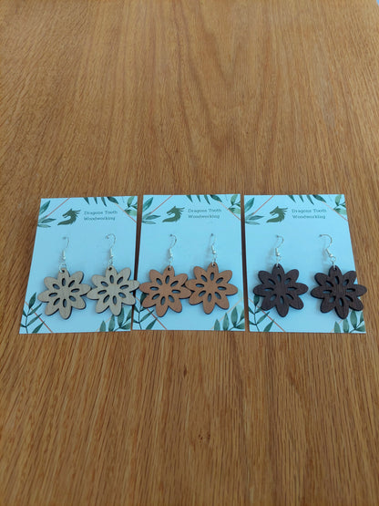 A beautiful collection of handcrafted wooden daisy flower dangle earrings displayed together in natural maple, cherry, and walnut woods.