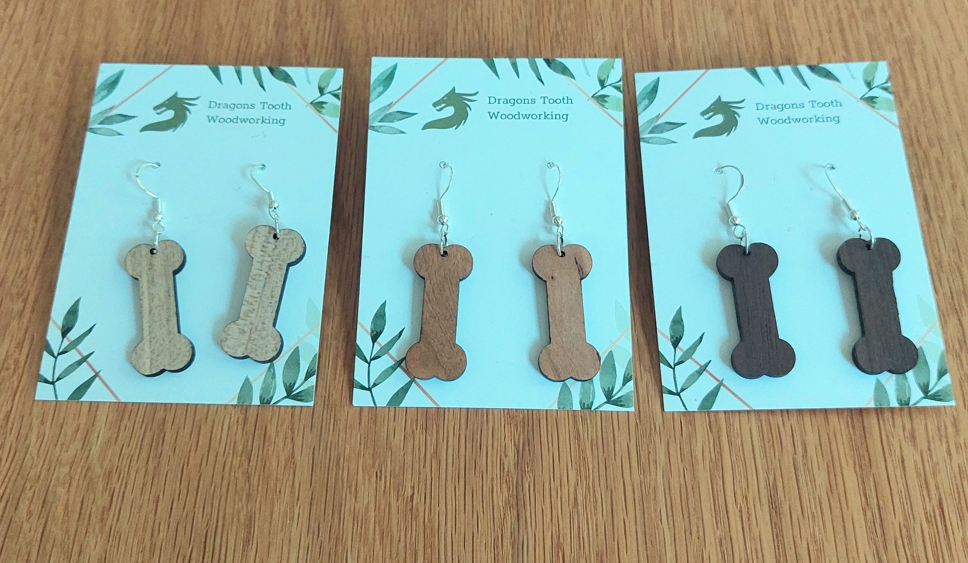 A beautiful lineup of handcrafted wooden dog bone dangle earrings displayed in natural maple, cherry, and walnut hardwoods.