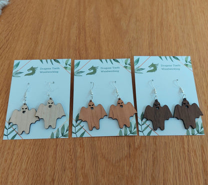 A collection of handcrafted wooden ghoul ghost dangle earrings displayed in natural maple, cherry, and walnut hardwood finishes.