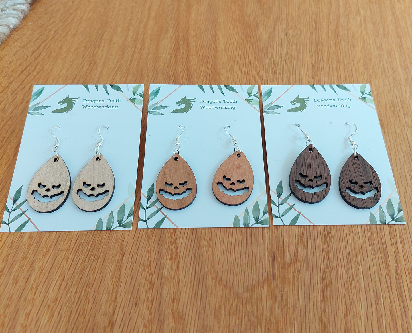 A beautiful collection of handcrafted wooden jack-o-lantern pumpkin teardrop dangle earrings displayed in cherry, maple, and walnut woods.
