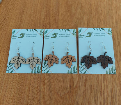 A collection of handcrafted wooden maple leaf dangle earrings shown in natural maple, cherry, and walnut woods on display.