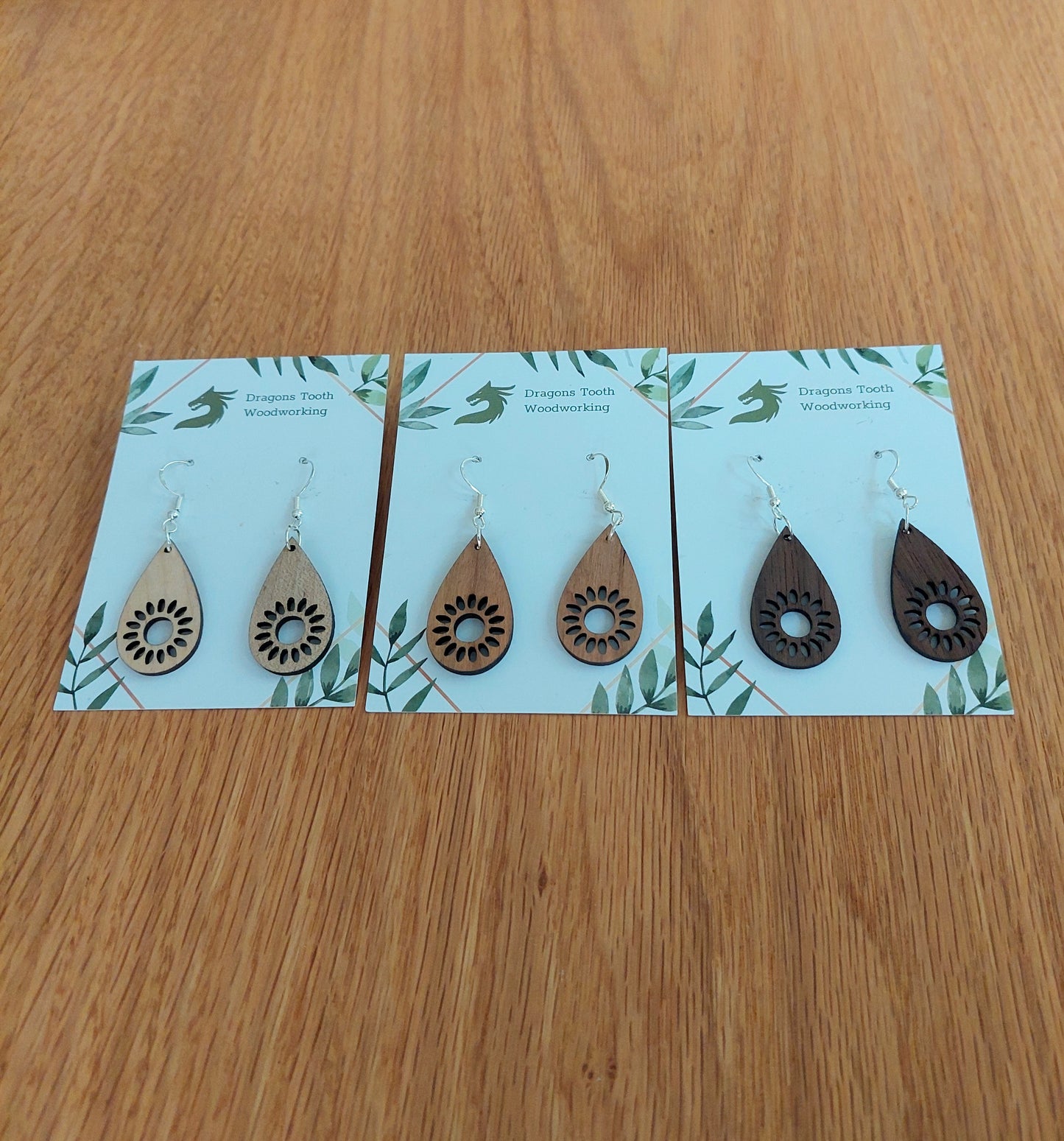 A beautiful collection of handcrafted wooden sunflower dangle earrings displayed together in natural cherry, maple, and walnut hardwood finishes.
