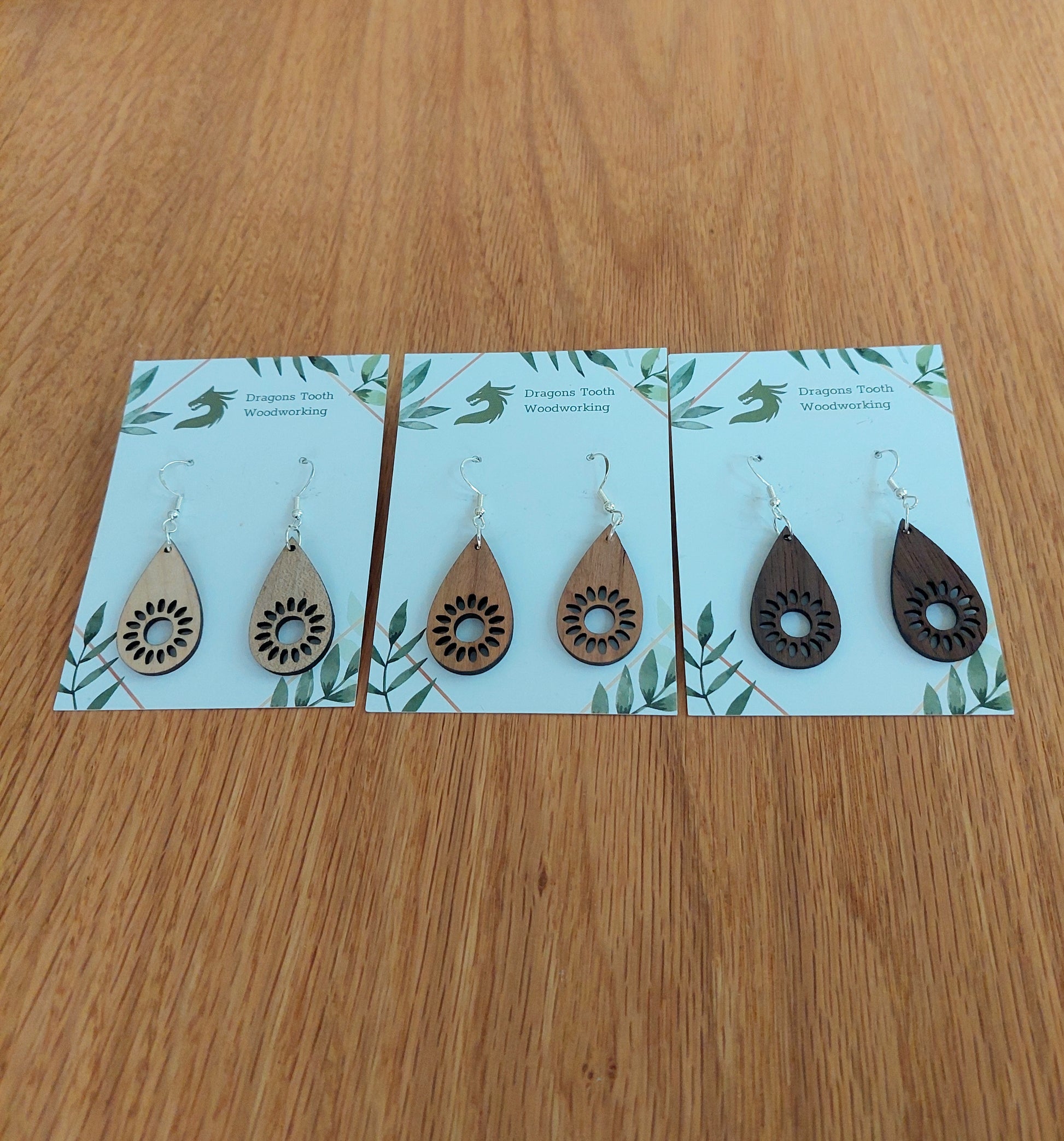 A beautiful collection of handcrafted wooden sunflower dangle earrings displayed together in natural cherry, maple, and walnut hardwood finishes.